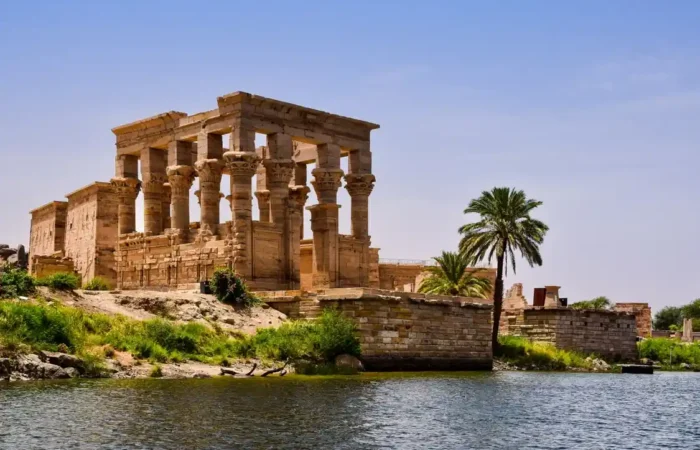 The historic Philae Temple in Aswan surrounded by the waters of the Nile River during sunset.