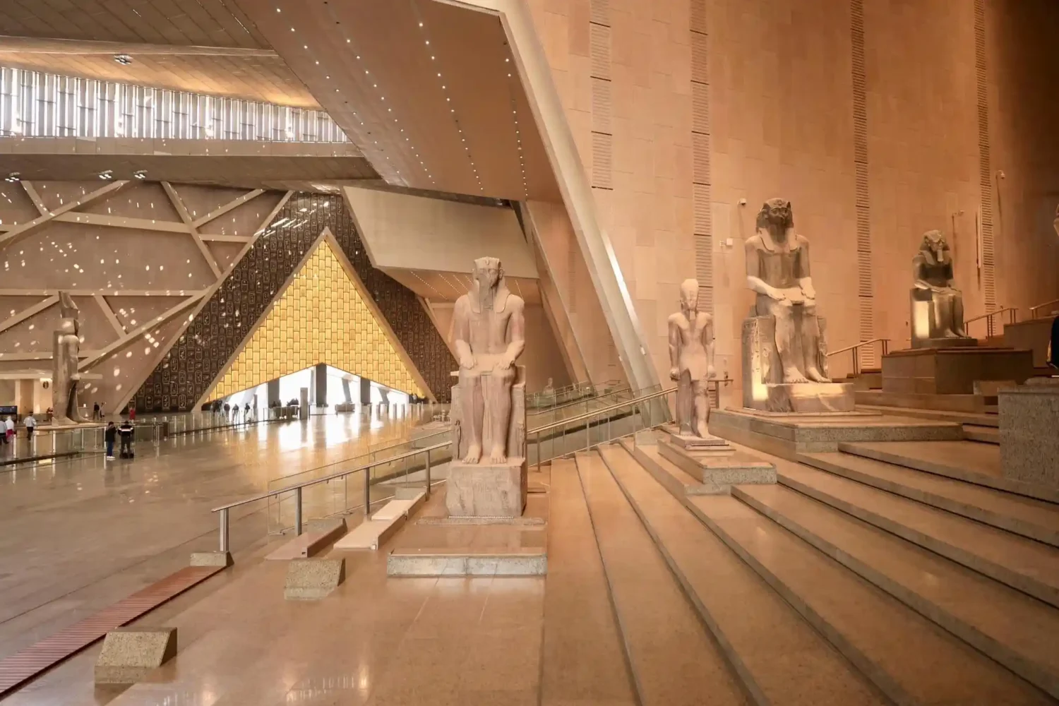 The iconic grand staircase entrance of the Grand Egyptian Museum GEM showing historic statues.